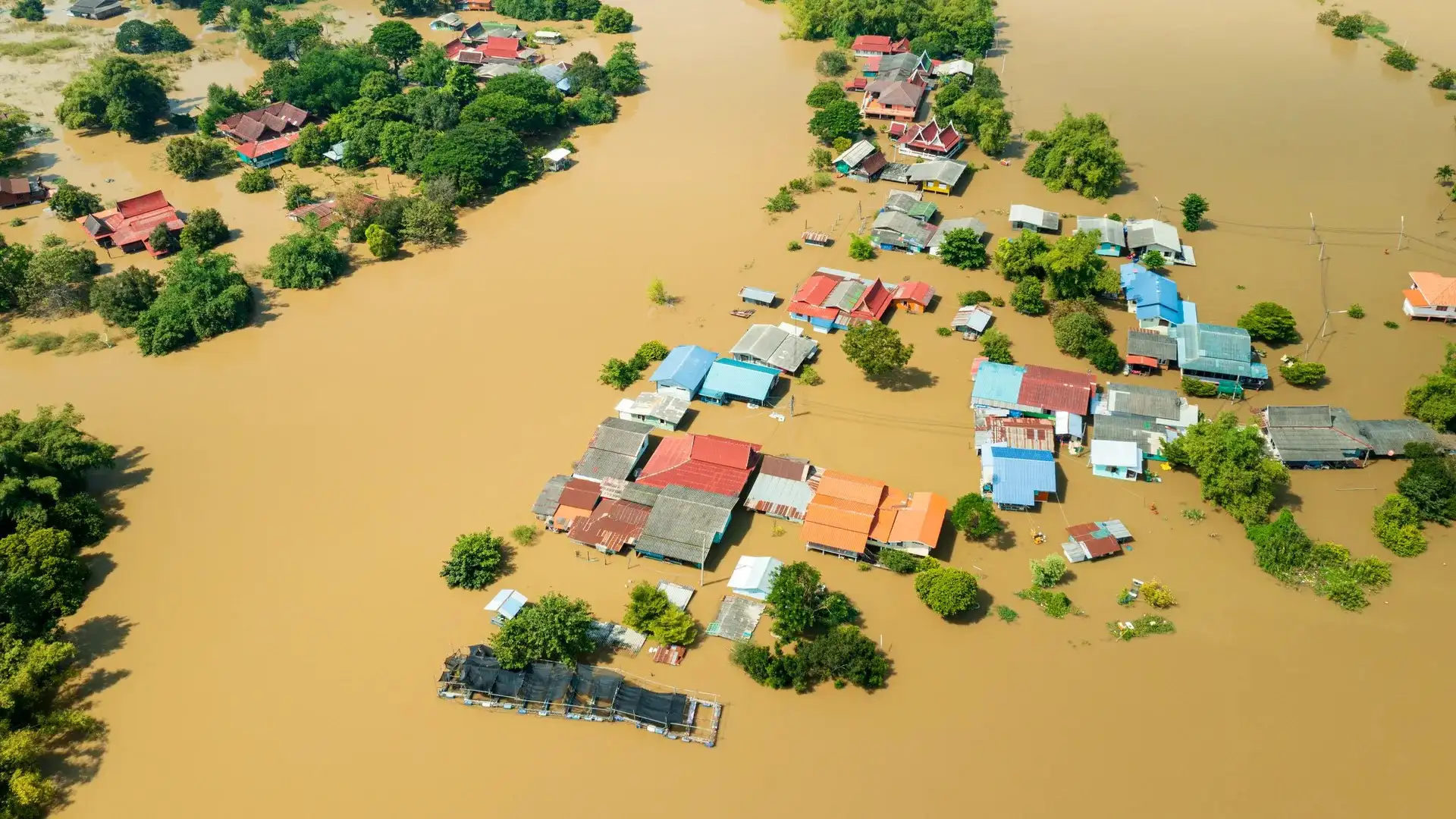 Vista aérea de un pueblo inundado, con viviendas y árboles parcialmente cubiertos por el agua, reflejando la magnitud de un episodio de inundación extrema.